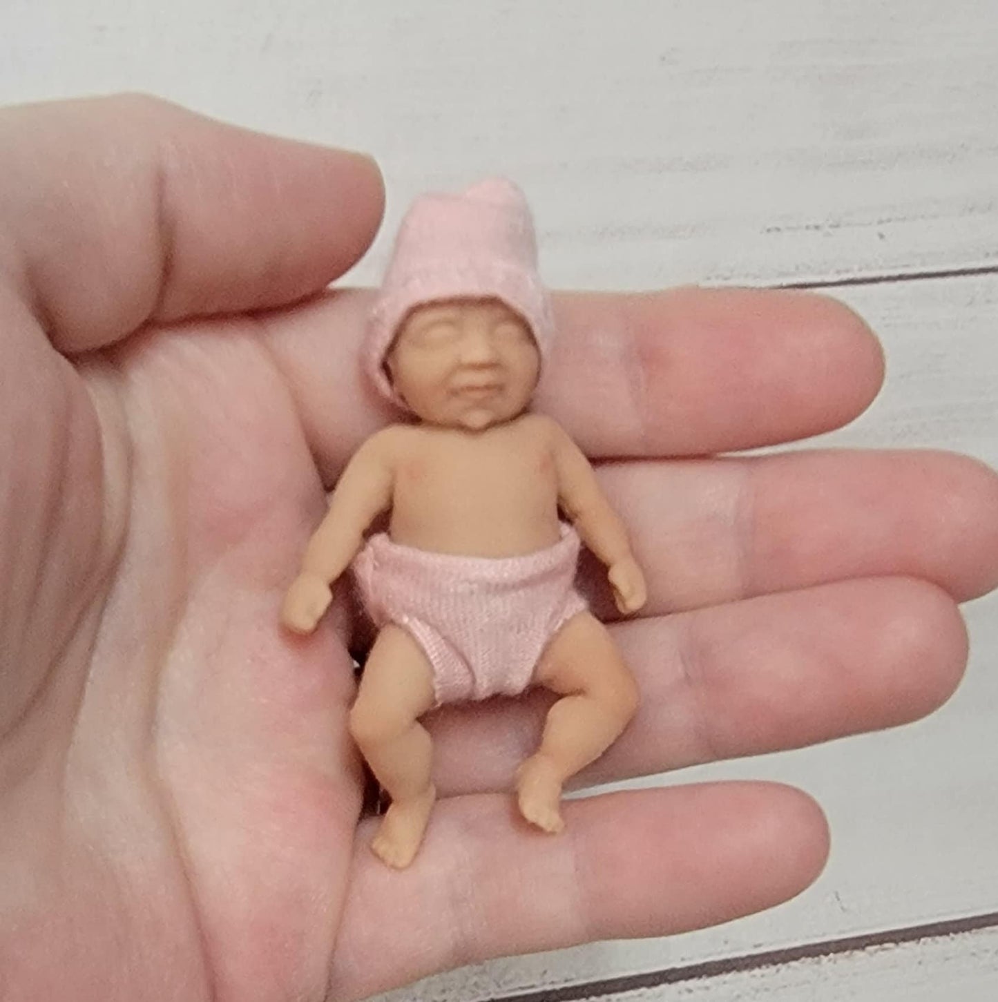 May include: A small pink baby doll wearing a pink hat and diaper.