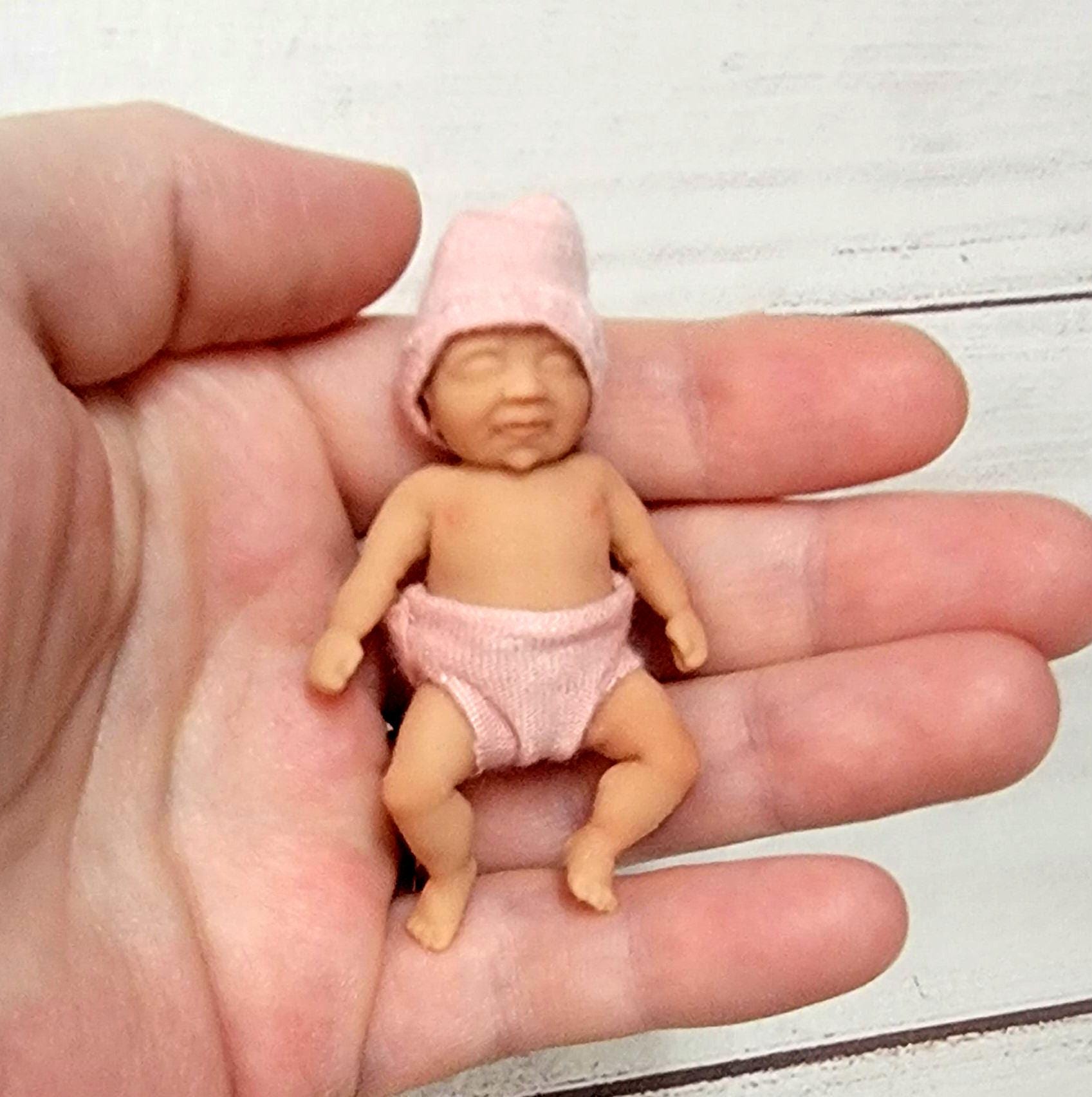 May include: A small pink baby doll wearing a pink hat and diaper.