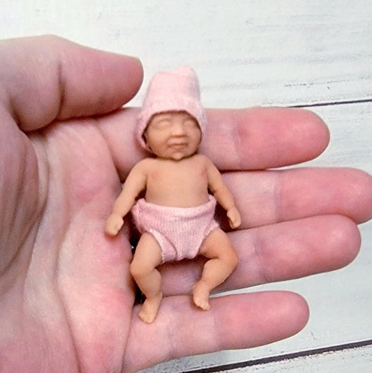 May include: A small pink baby doll wearing a pink hat and diaper.